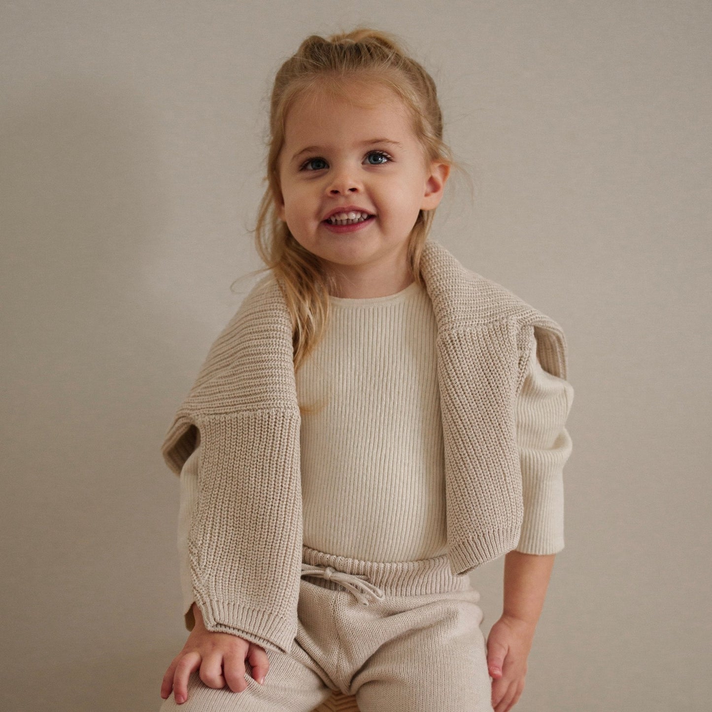 Child wearing a beige knit cardigan and pants against a plain background