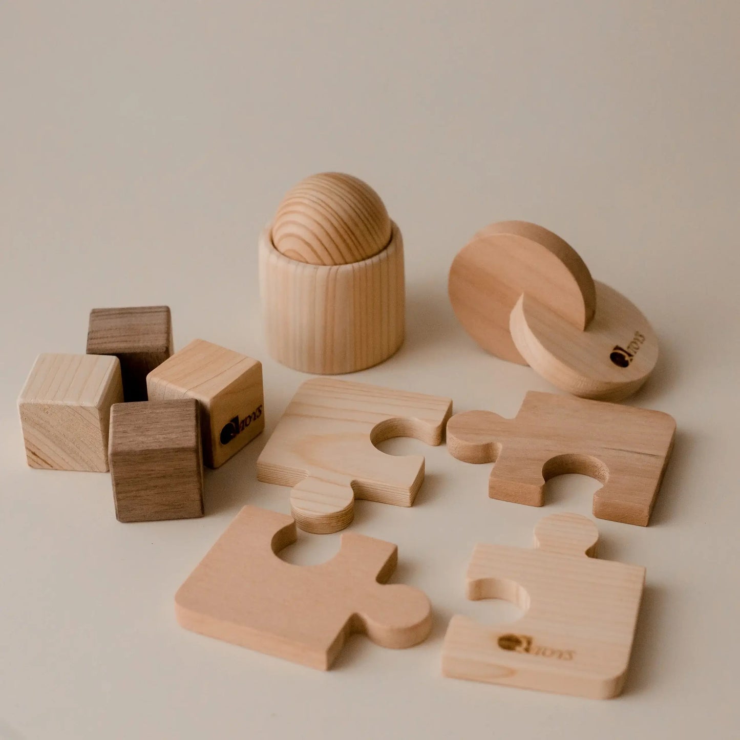 Set of wooden toys including a cup with ball, dual discs, blocks and a puzzle on a beige background