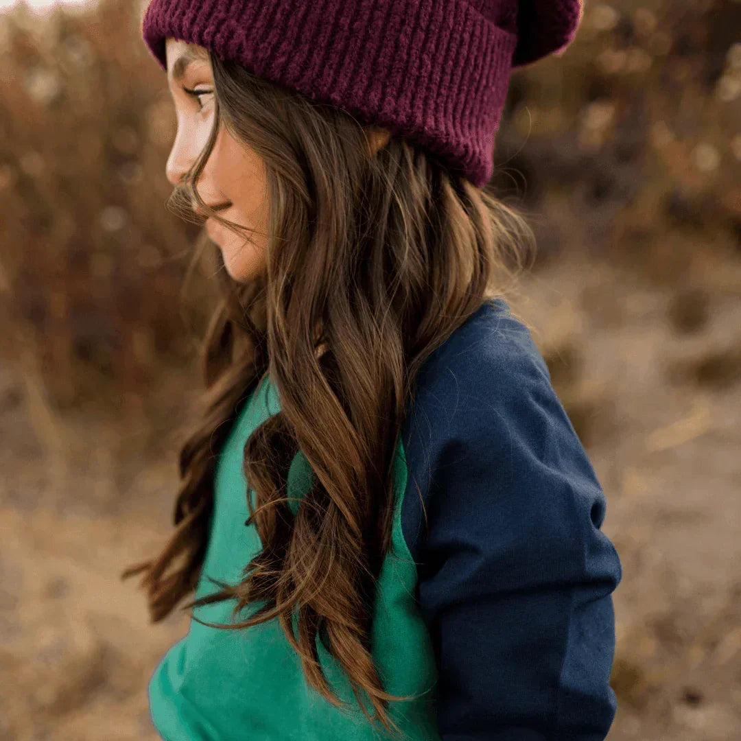 Child wearing a purple beanie and blue jacket in a natural setting
