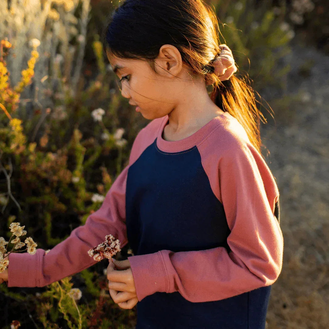 Young girl in a pink and navy sweater holding flowers in a natural setting