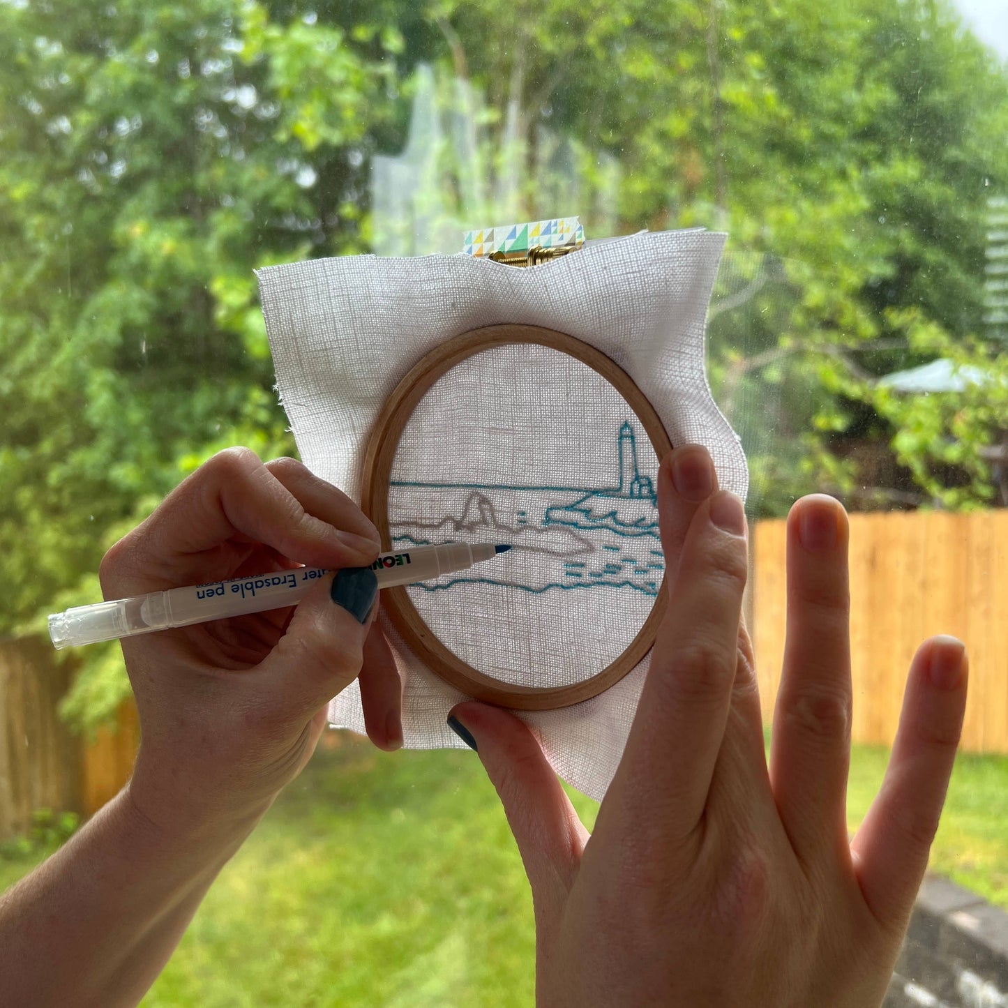 Person holding an embroidery hoop and tracing a design pattern outdoors.