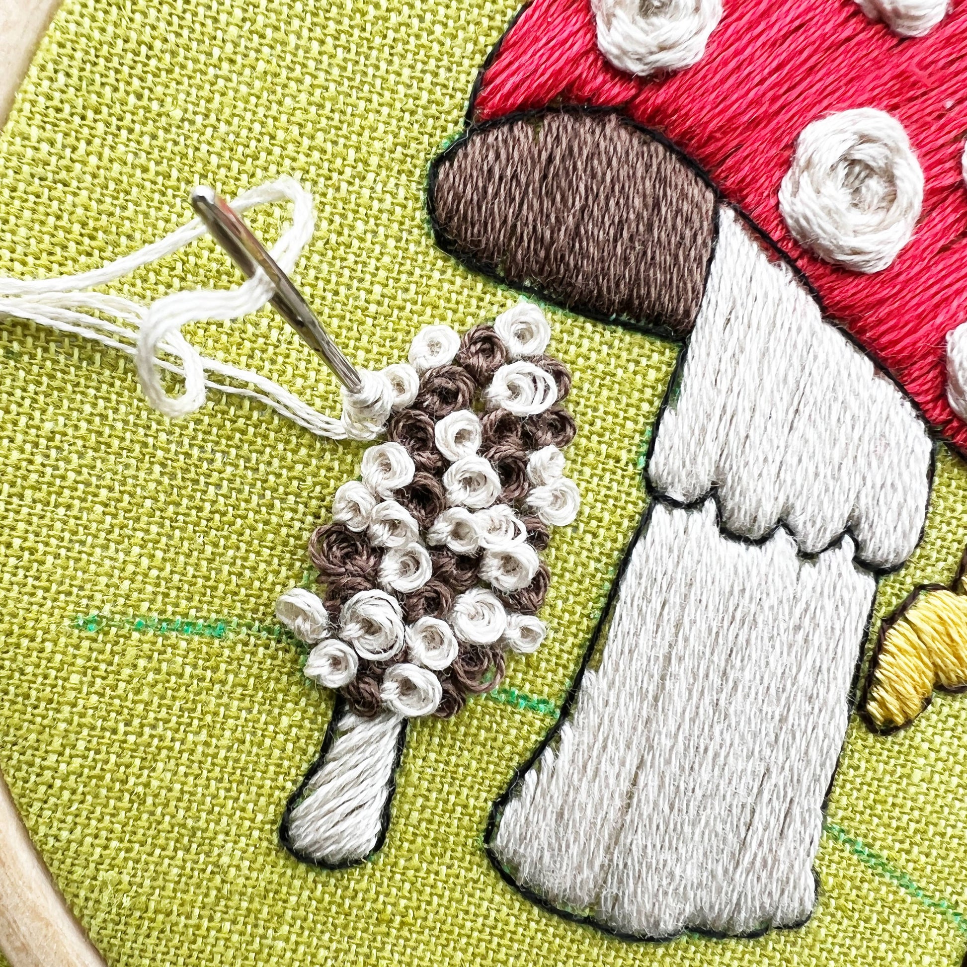 Embroidery hoop with a mushroom and hedgehog design on green fabric.