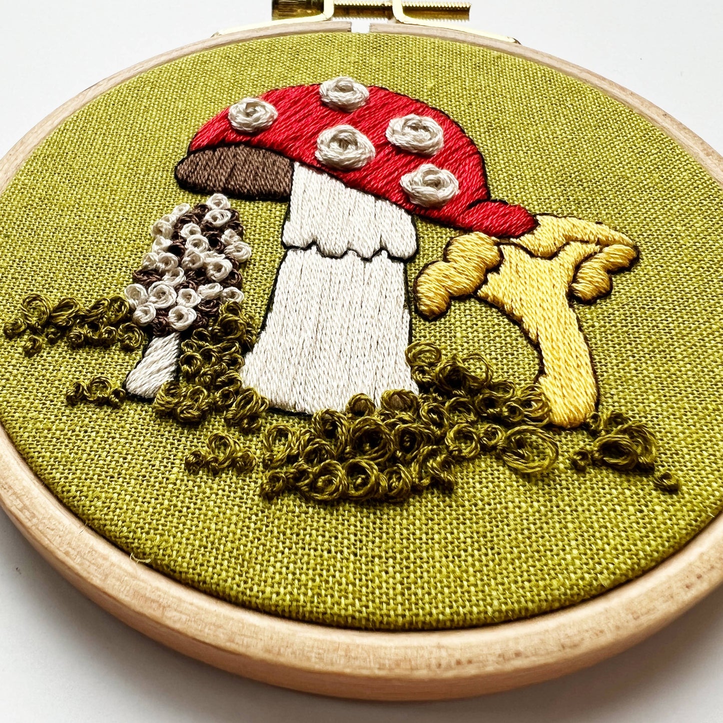 Embroidery hoop with embroidered mushrooms on green fabric