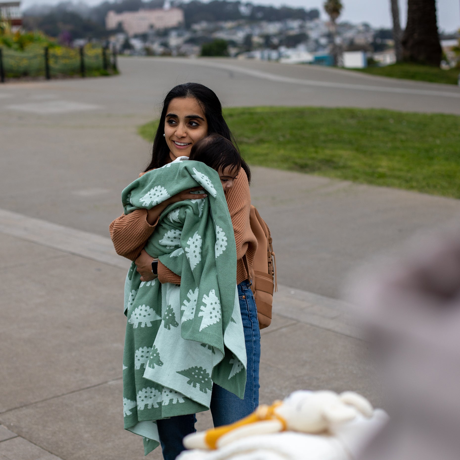 Woman holding a green blanket with white patterns on a sidewalk