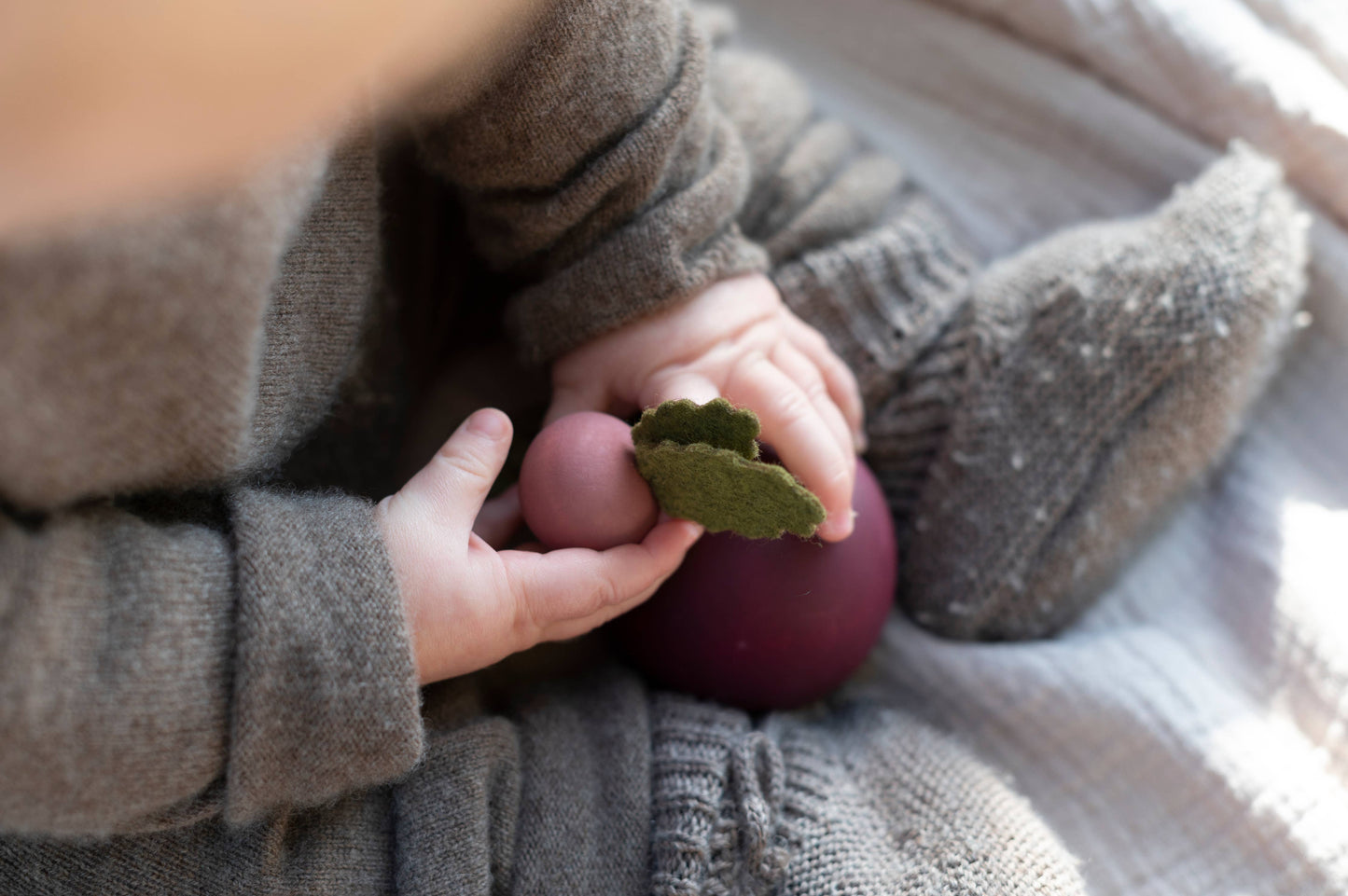 a toddler sitting on a bed playing with wooden radish and beet