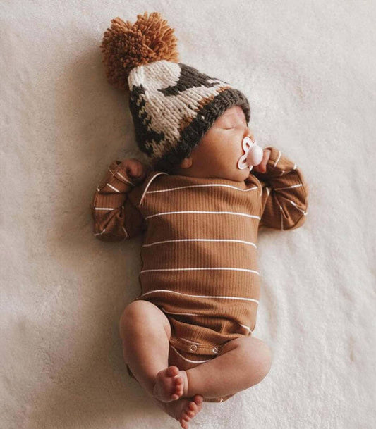 Newborn baby wearing a striped onesie and knitted hat with a pom-pom on a soft surface.