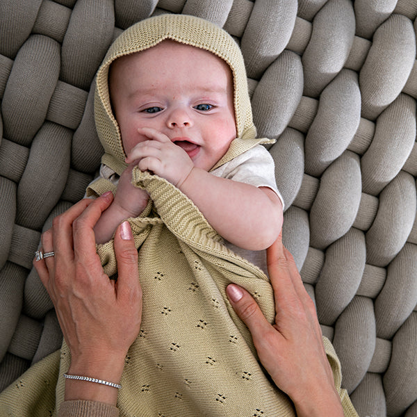 Baby wearing a beige knitted outfit lying on a textured surface