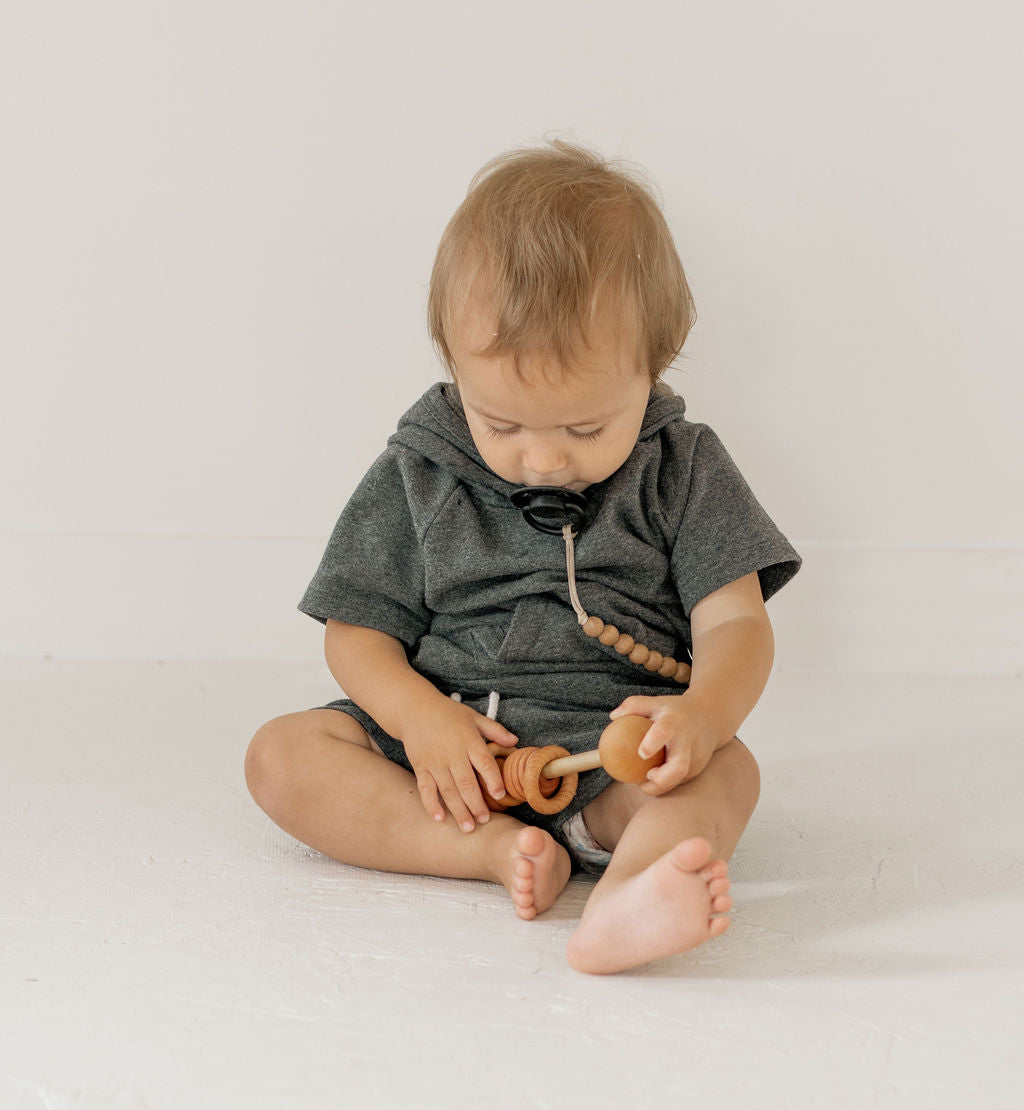 Baby in a dark gray outfit playing with wooden toys on a light background