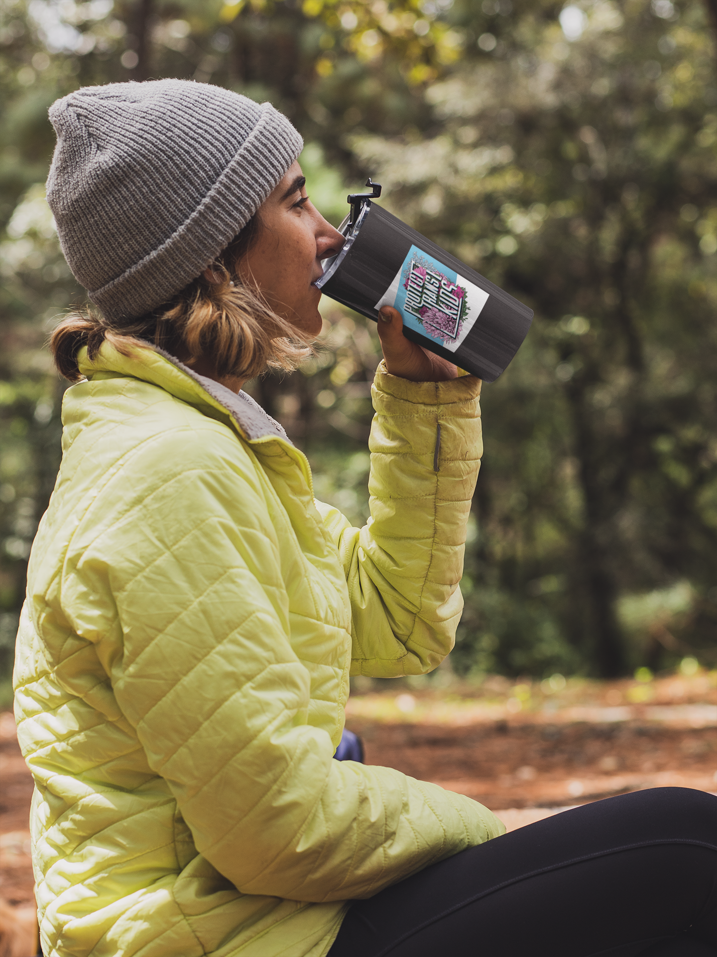 a person sitting outdoors drinking from a tumbler with 4x5 art Stickers by artist Rae Senarighi (aka Transpainter) that read "Protect Trans Kids" on a blue and white surrounded by pink, blue, and white florals inspired by the transgender pride flag on it