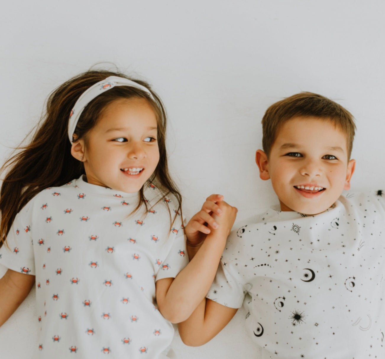 Two children holding hands and smiling against a white background