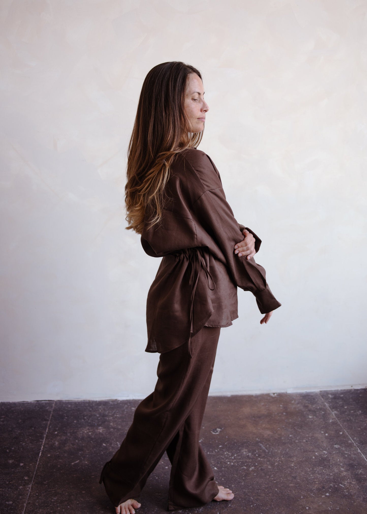 Woman wearing a brown outfit standing against a white wall.