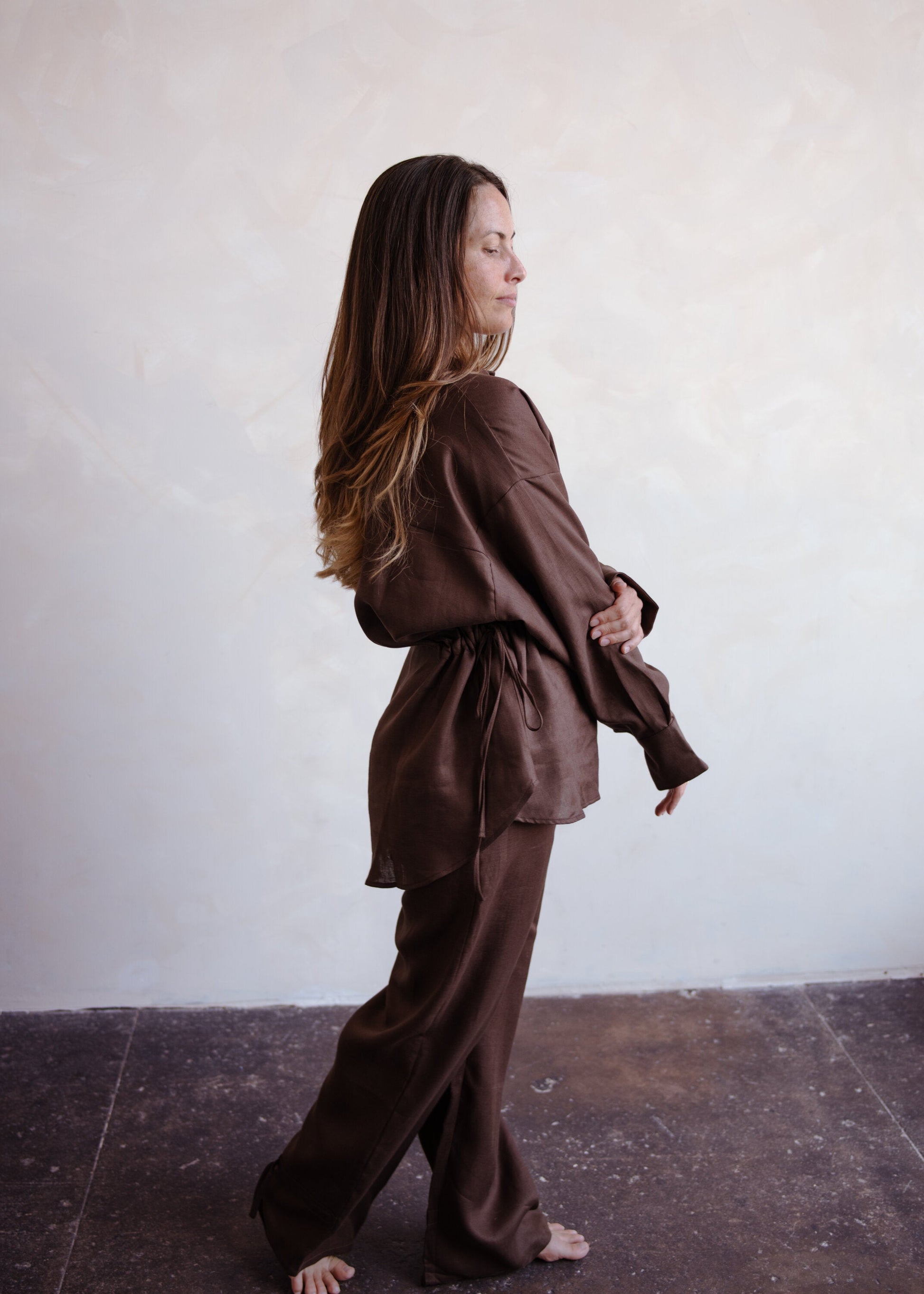 Woman wearing a brown outfit standing against a white wall.