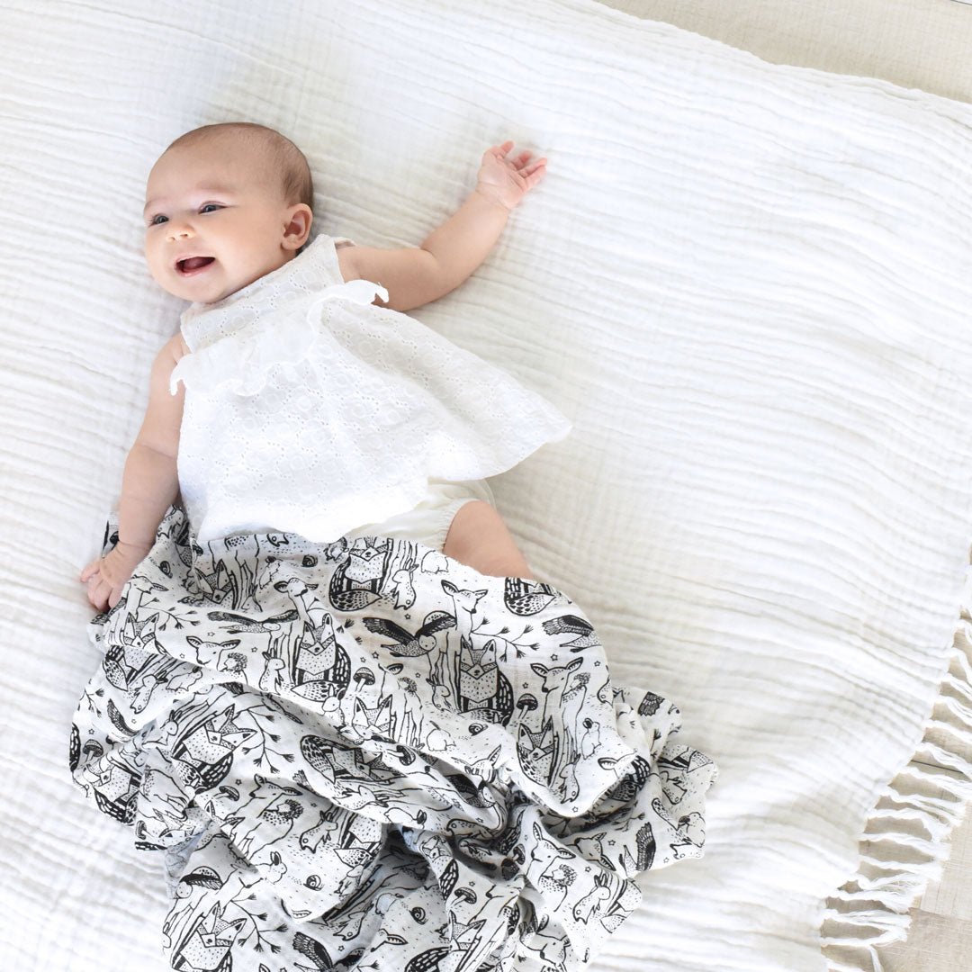Baby lying on a white textured blanket wearing a white outfit with black patterns.
