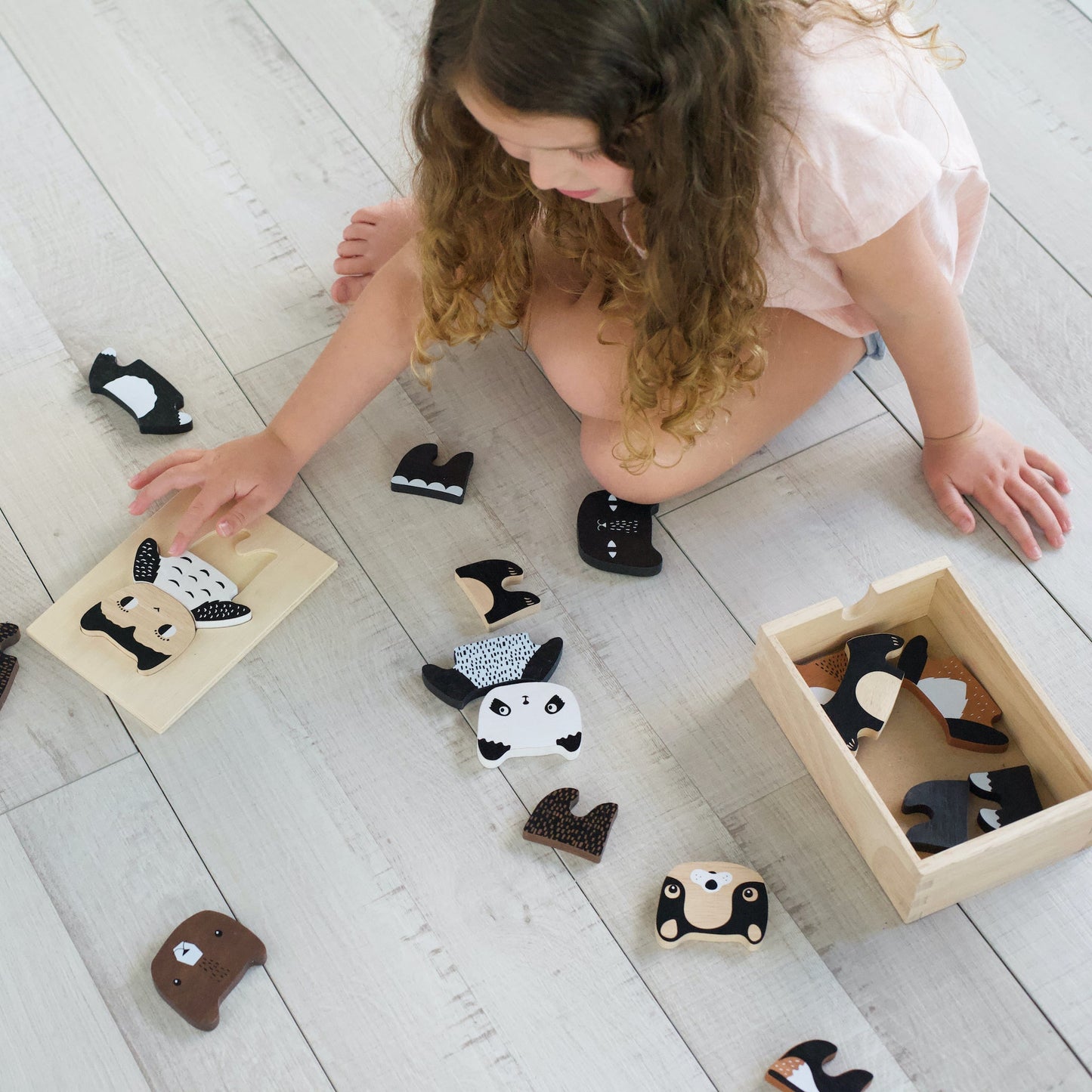 Child playing with animal-shaped wooden toys on a light wooden floor.