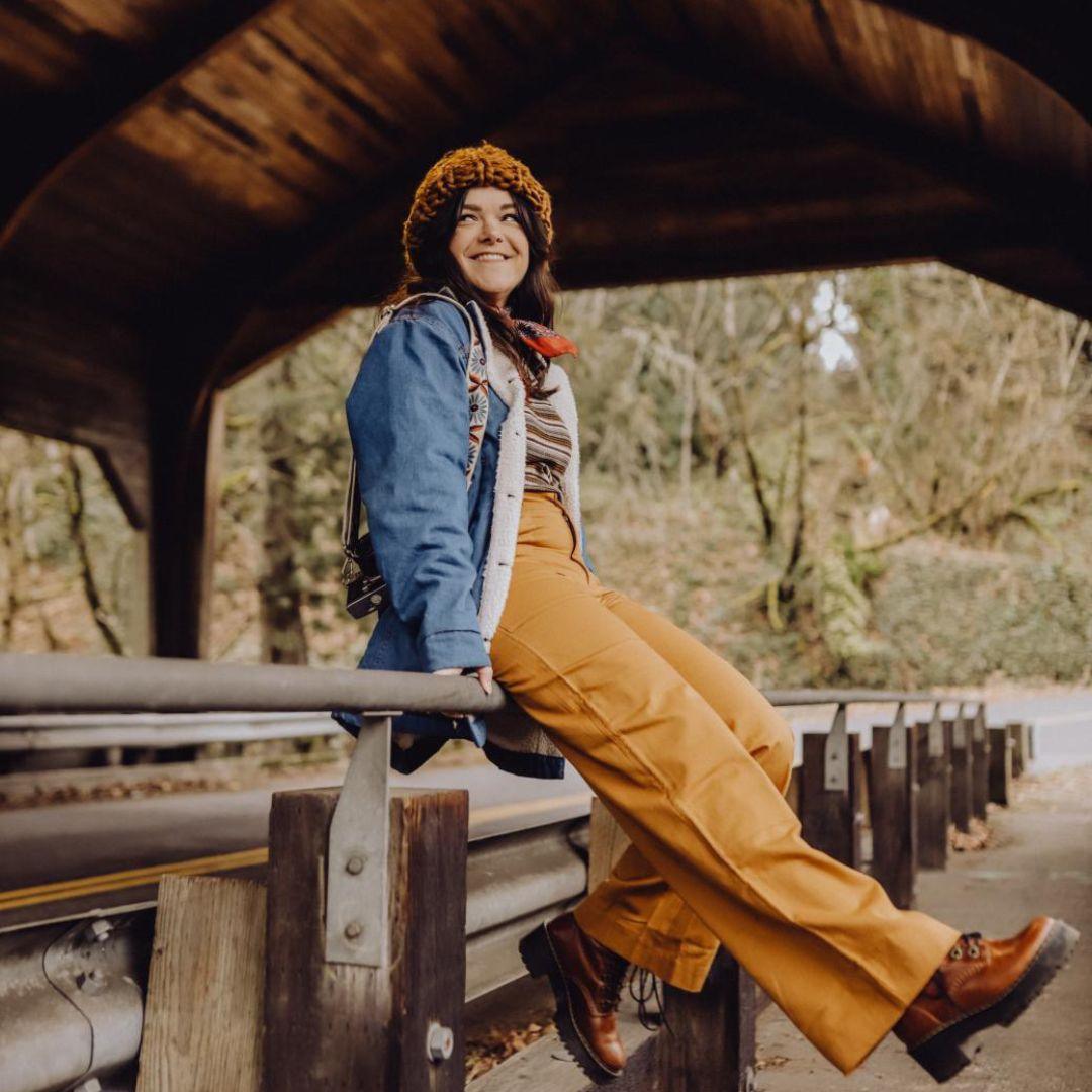 Woman sitting on a wooden bench under a covered bridge with trees in the background
