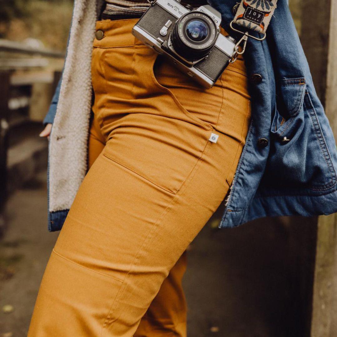 Person wearing mustard pants and a denim jacket with a camera on a blurred background
