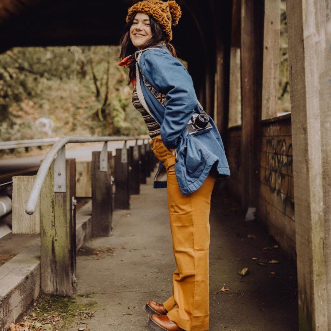 Woman in blue jacket and yellow pants standing on a wooden bridge