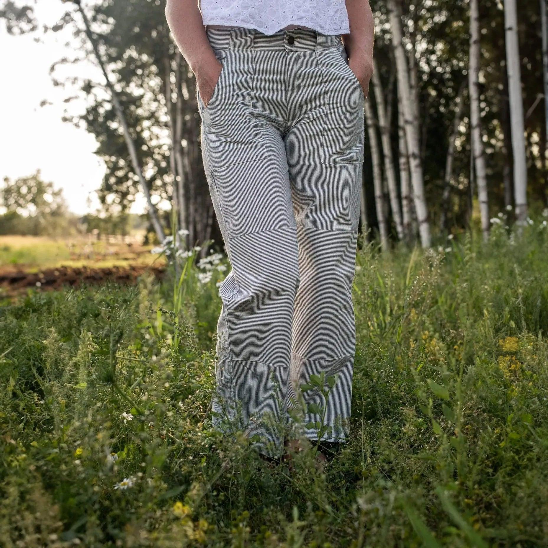Person wearing light-colored pants standing in a grassy field with trees in the background