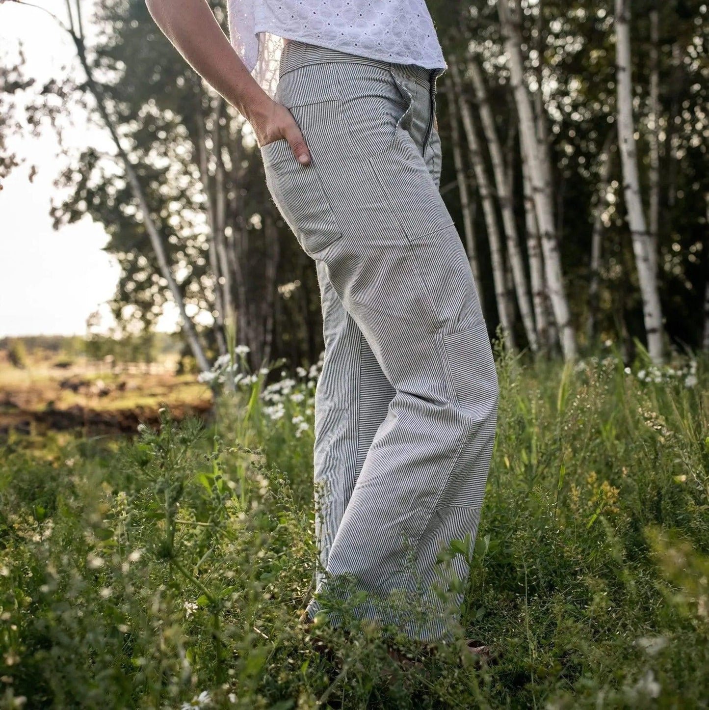 Person wearing light gray pants standing in a grassy field with trees in the background