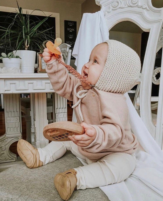 a baby sitting on a chair holding a Natural Rubber Round Pacifier